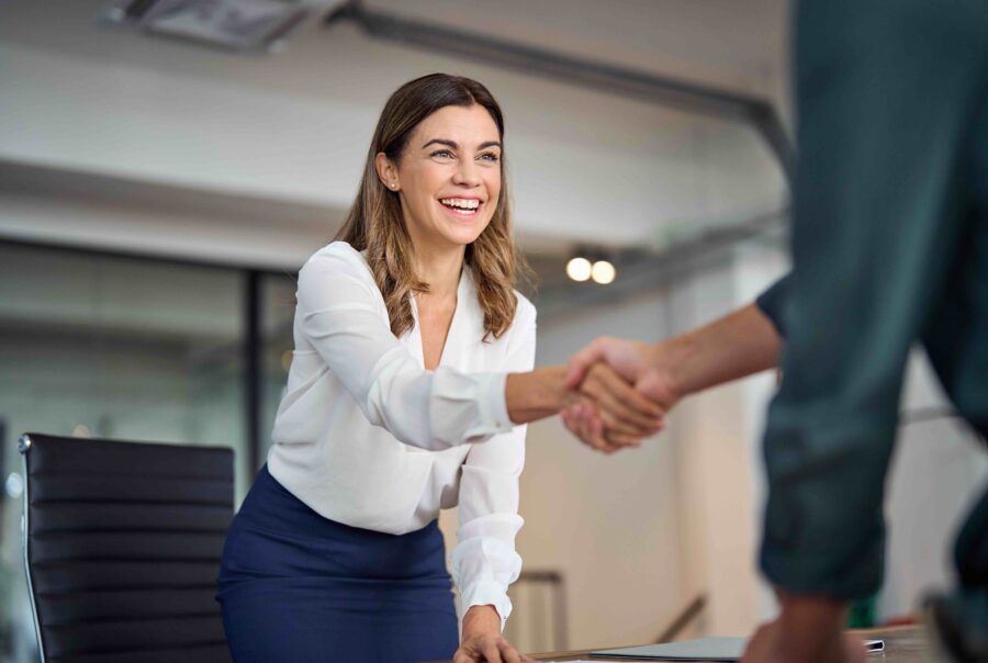 Happy mid aged business woman manager handshaking greeting client in office